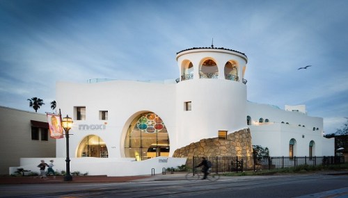 A modern white building with unique architectural features, featuring large windows and a stone base, set against a twilight sky.