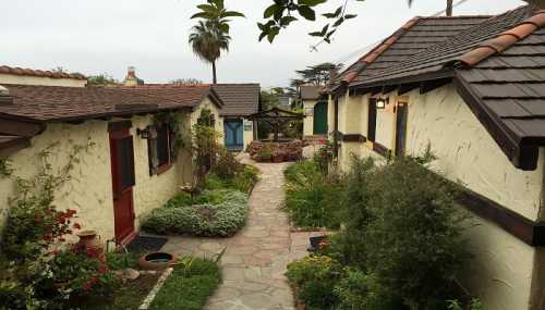 A charming pathway lined with small cottages and lush greenery, leading to a garden area under a cloudy sky.