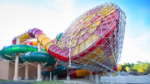 Colorful water slides twist and turn around a large, geometric structure against a clear blue sky.