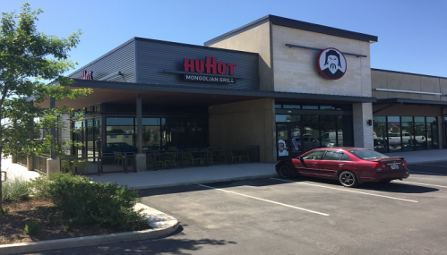 Exterior of a HuHot Mongolian Grill restaurant with a red car parked in front and clear blue skies.