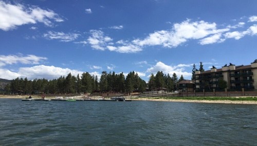 A serene lake scene with a dock, boats, and a forested shoreline under a blue sky with fluffy clouds.