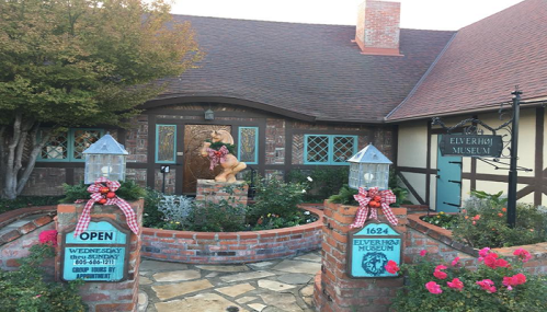 A charming museum entrance with brick walls, festive decorations, and a statue, surrounded by greenery.