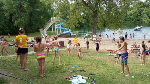 Children playing with hula hoops by a beach, with a water slide and people swimming in the background.