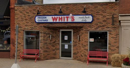 Exterior of Whit's Frozen Custard shop, featuring a brick facade, sign, and red benches outside.