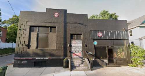 A black brick building with large windows and a sign reading "Respect the Artist, Their Work" in front.