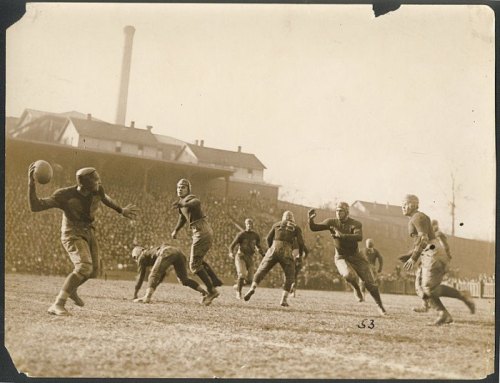 Historic black-and-white photo of a football game, with players in vintage uniforms on a grassy field.