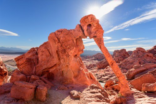 A striking rock formation in a desert landscape, with vibrant red hues and a bright blue sky above.