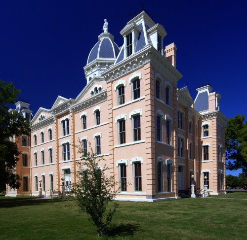 Historic pink building with a dome, surrounded by green grass and trees under a clear blue sky.