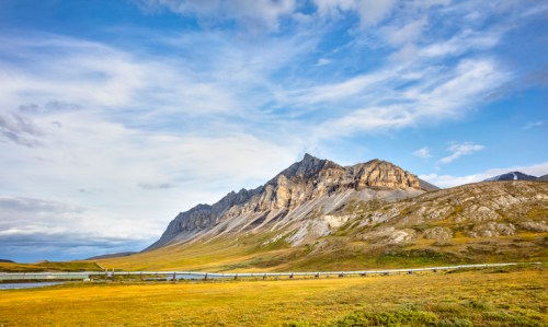 A scenic landscape featuring a mountain range under a cloudy sky, with a grassy foreground and a winding path.