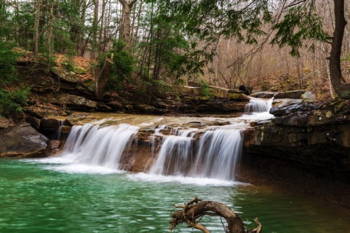 A serene waterfall cascades into a turquoise pool, surrounded by lush greenery and rocky terrain.