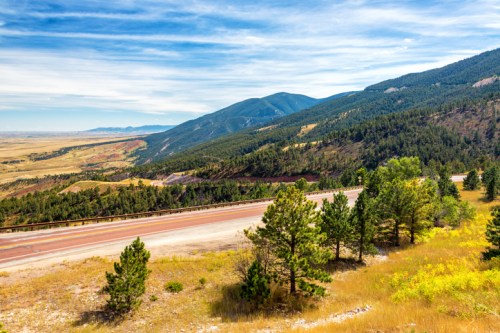 Scenic view of mountains and a winding road, surrounded by lush greenery and blue skies.