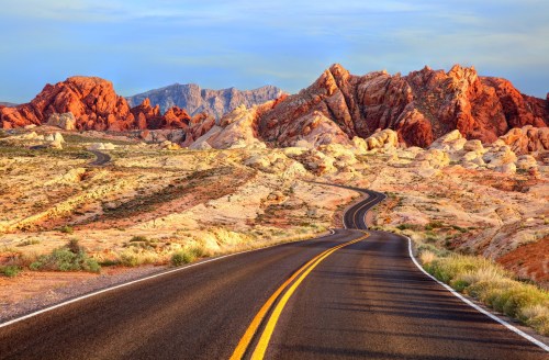 Winding road through colorful rock formations and desert landscape under a clear sky.