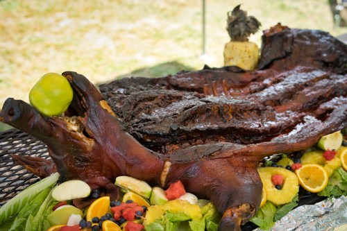 A roasted pig head garnished with fruits and vegetables, displayed on a grill.