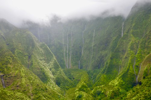 Lush green mountains with cascading waterfalls, shrouded in mist and clouds.