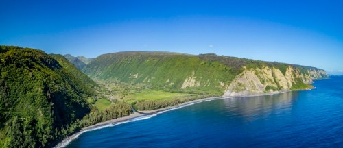 A panoramic view of a lush green coastline with cliffs, clear blue water, and a bright blue sky.