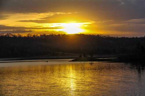 Sunset over a calm lake, with golden reflections on the water and silhouettes of trees in the background.