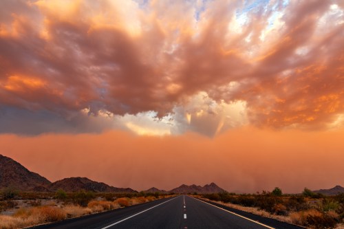 A deserted road stretches into the distance under a dramatic sky filled with colorful clouds at sunset.