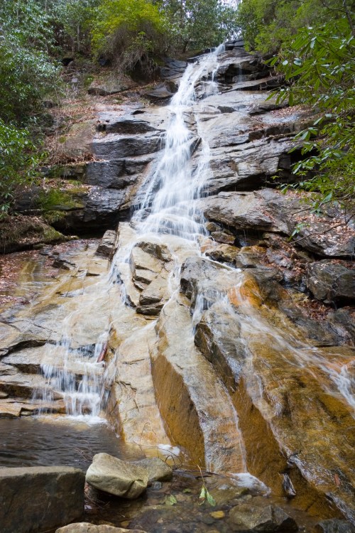 A cascading waterfall flows over rocky terrain, surrounded by lush greenery and trees.