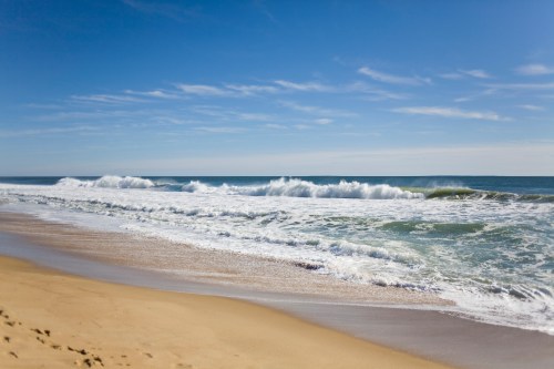Waves gently crashing on a sandy beach under a clear blue sky.