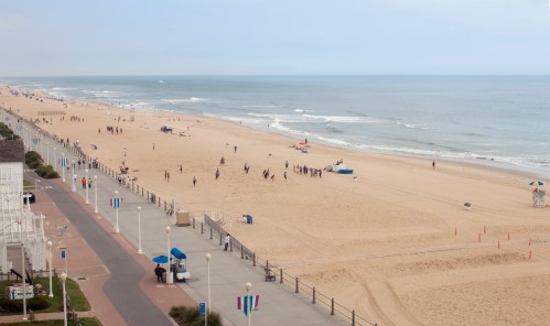 A wide view of a sandy beach with people enjoying the shore, gentle waves, and a cloudy sky in the background.