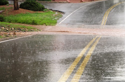 A wet road with yellow lines, showing heavy rain and pooling water from recent downpours.