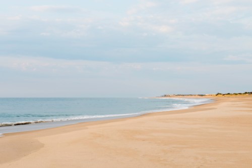 A serene beach with soft sand, gentle waves, and a cloudy sky stretching into the distance.