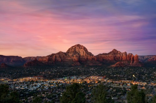 A scenic view of mountains at sunset, with a town illuminated below and colorful clouds in the sky.