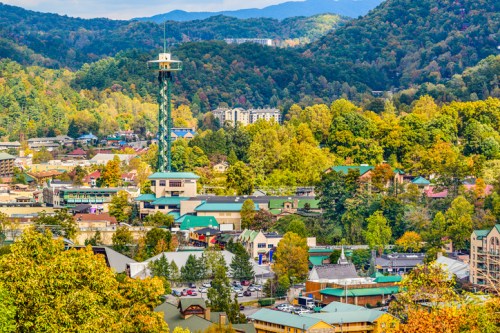 A scenic view of a mountain town with colorful trees, buildings, and a tall observation tower in the background.