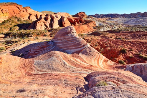 Colorful, layered rock formations in a desert landscape under a clear blue sky.