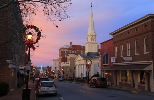 A charming street scene at dusk, featuring a church steeple, festive decorations, and a colorful sky.