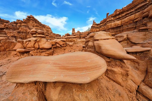 A rocky landscape featuring unique, smooth rock formations under a blue sky with scattered clouds.