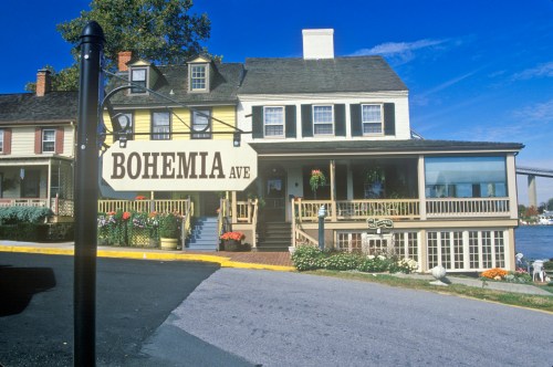 A charming building with a sign reading "Bohemia Ave," featuring a porch and colorful flowers under a clear blue sky.