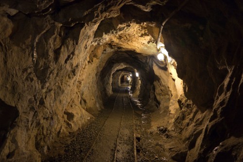 A dimly lit underground tunnel with rocky walls and railway tracks running through it.