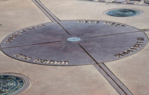 A circular stone plaque on the ground with engraved text and symbols, marking a meeting point.