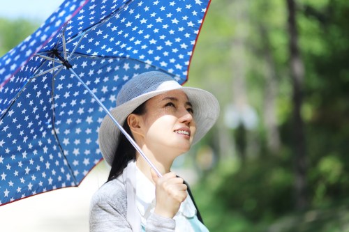A woman in a sun hat holds a blue star-patterned umbrella, looking up with a smile on a sunny day.