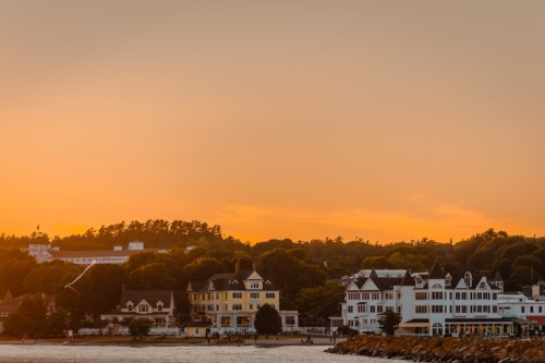 Sunset over a coastal town with historic buildings and lush greenery along the shoreline.