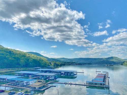 A serene lake view with floating docks, surrounded by green hills and a blue sky with fluffy clouds.