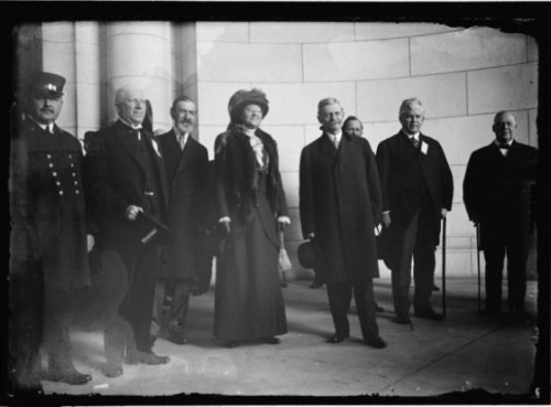 A group of men and a woman in formal attire pose together indoors, with a police officer on the left.