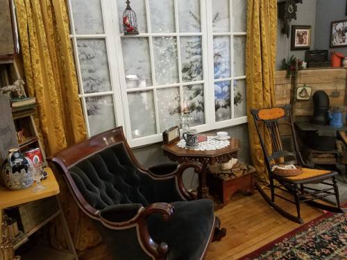 Cozy room with a velvet armchair, rocking chair, and festive window view, adorned with warm curtains and vintage decor.