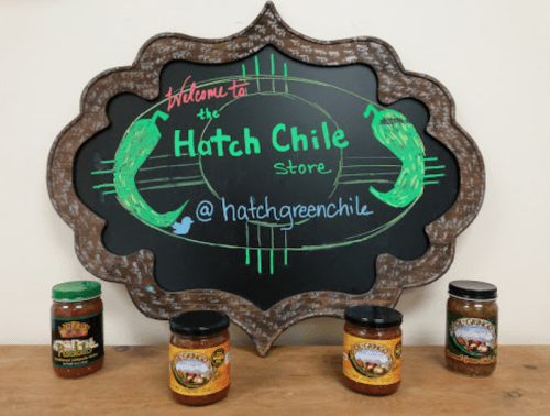 Chalkboard sign for the Hatch Chile Store with jars of salsa displayed in front.