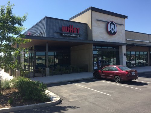Exterior of a HuHot Mongolian Grill restaurant with a red car parked in front and clear blue skies.