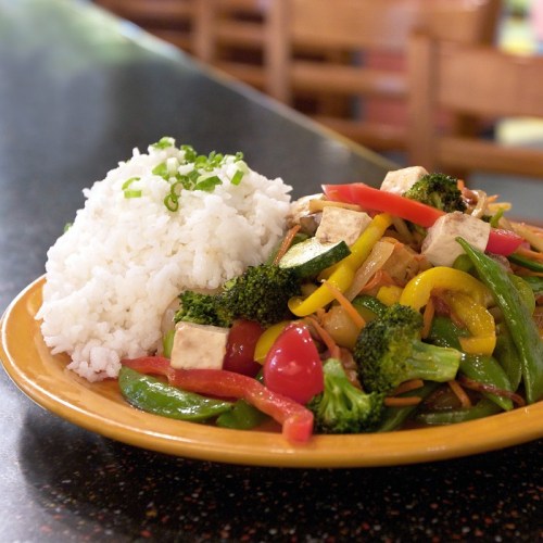 A plate of colorful vegetable stir-fry with tofu, served alongside a portion of white rice.