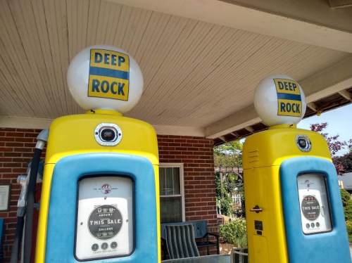 Two vintage gas pumps with yellow and blue colors, labeled "DEEP ROCK," under a covered area.