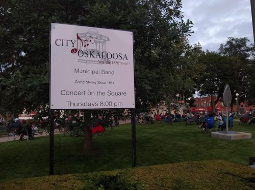 Sign for a concert by the Oskaloosa Municipal Band, held on Thursdays at 8:00 PM in the town square.