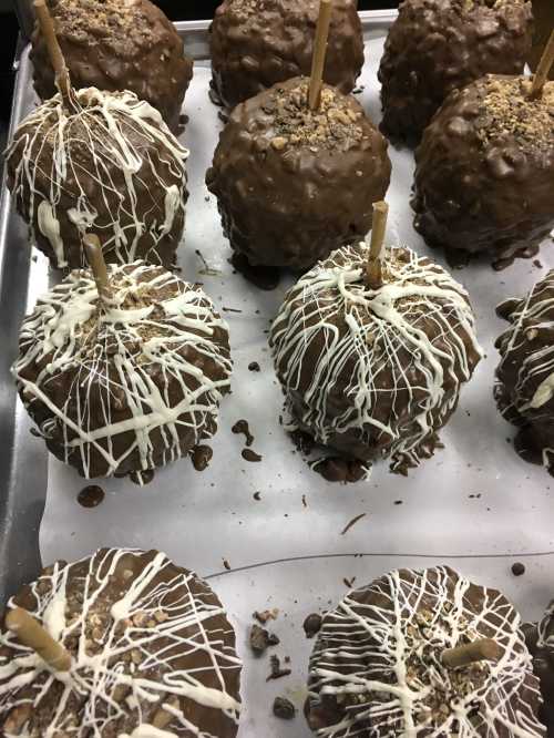 A tray of chocolate-covered apples drizzled with white chocolate and topped with crushed nuts.