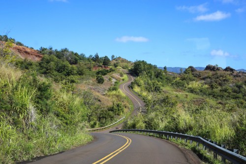 Winding road through lush green hills under a clear blue sky.