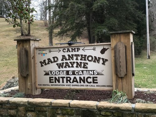 Sign for Camp Mad Anthony Wayne Lodge & Cabins, featuring "Entrance" and contact information, surrounded by trees.