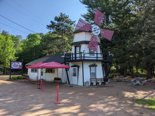 A whimsical ice cream shop with a windmill design, surrounded by trees and picnic tables on a sunny day.