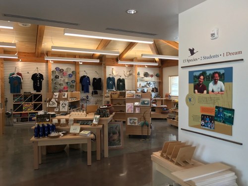 Interior of a gift shop with merchandise displays, including clothing and educational items, and a sign about a conservation program.