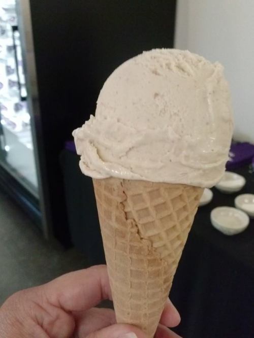 A hand holding a waffle cone filled with a scoop of light-colored ice cream.